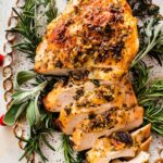 An air fryer turkey breast sliced sitting on a bed of fresh herbs and cranberries on a white platter.