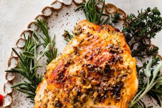 An air fryer turkey breast sliced sitting on a bed of fresh herbs and cranberries on a white platter.