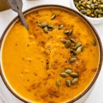 A bowl of autumn soup topped with cracked black pepper, and pepitas.