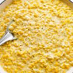 Creamed corn served in a white skillet with a silver spoon topped with freshly cracked pepper.