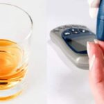 Glass of alcohol on a table and person checking their blood sugar