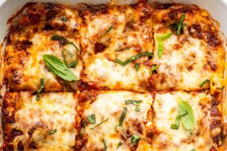 Healthy lasagna in a baking dish, cut into squares, and garnished with fresh basil and parsley.