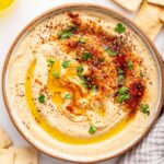 A bowl of creamy hummus topped with olive oil, herbs, and spices.