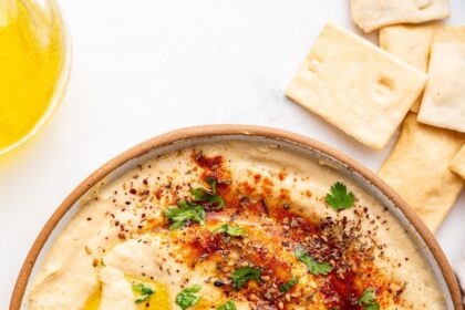 A bowl of creamy hummus topped with olive oil, herbs, and spices.