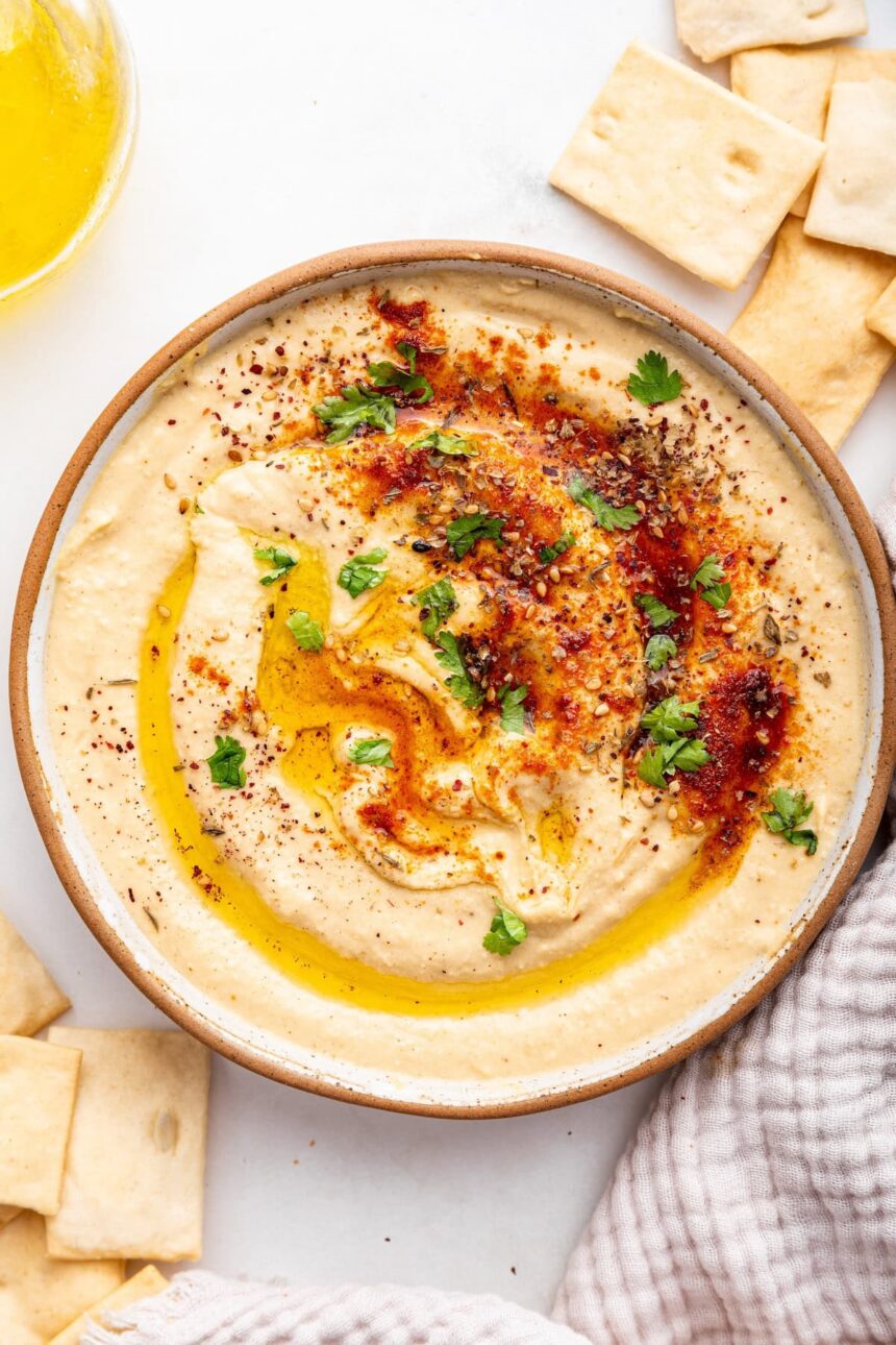 A bowl of creamy hummus topped with olive oil, herbs, and spices.