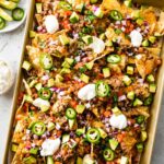 Loaded nachos on a baking tray with meat, jalapeños, sour cream, avocado, cheese, and more.