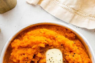 Mashed sweet potato in a bowl topped with two slices of butter and seasonings.