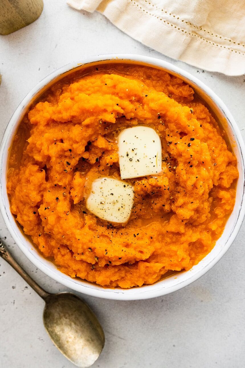 Mashed sweet potato in a bowl topped with two slices of butter and seasonings.