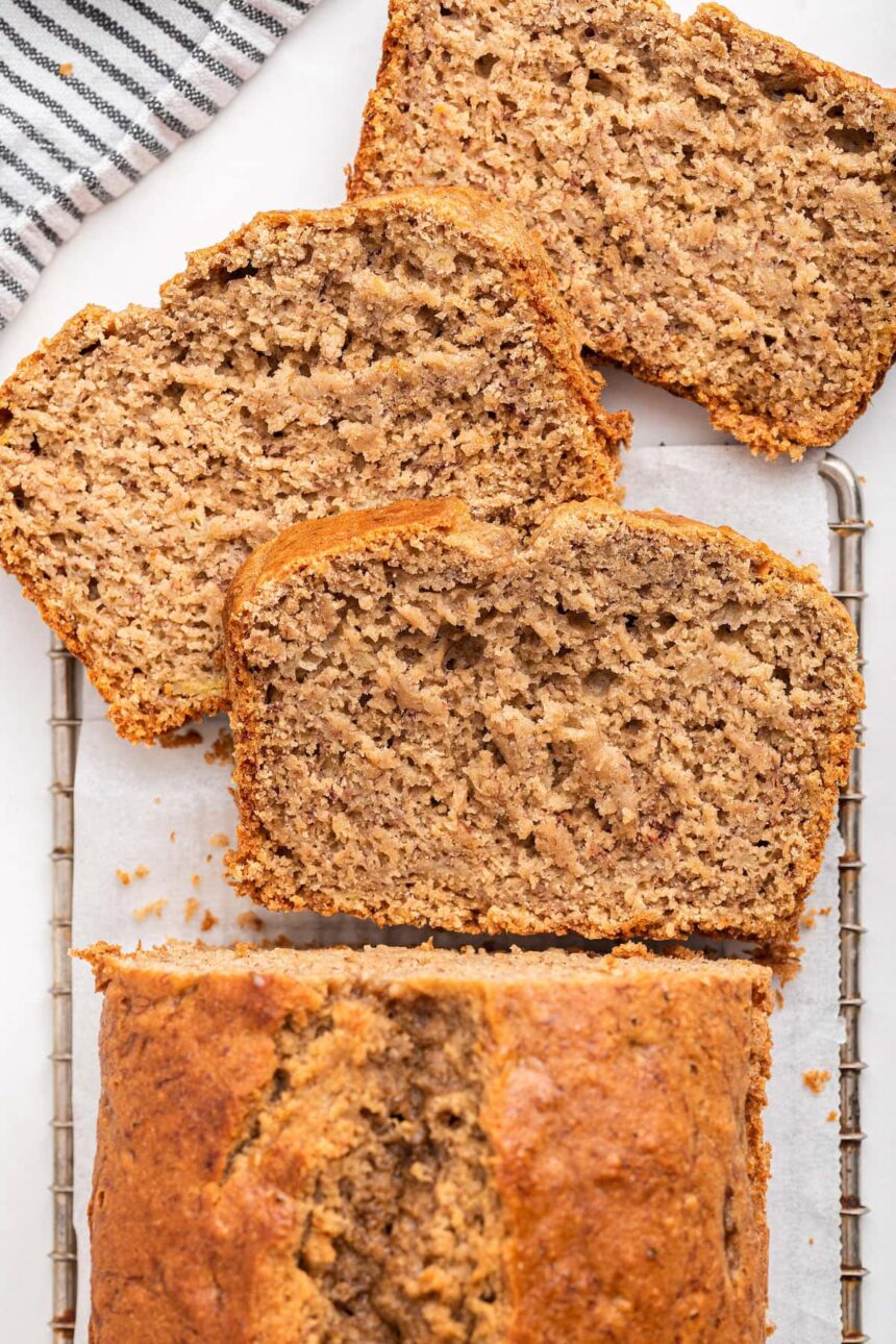 Oat flour banana bread on a cooling wire rack with three slices near the loaf.