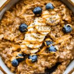 A bowl of peanut butter oatmeal topped with fresh banana slices, blueberries, a drizzle of peanut butter and chia seeds.