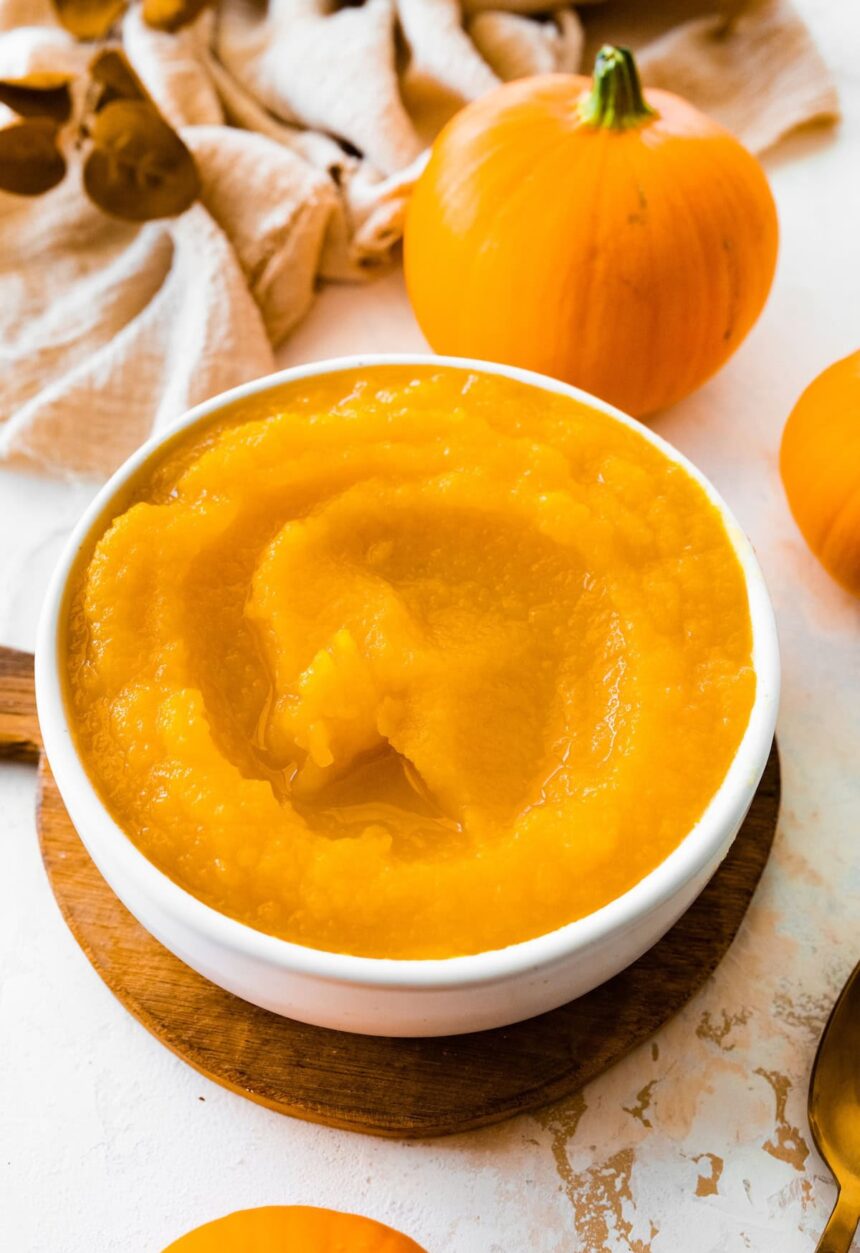 A homemade pumpkin puree in a bowl on a circular wooden board.