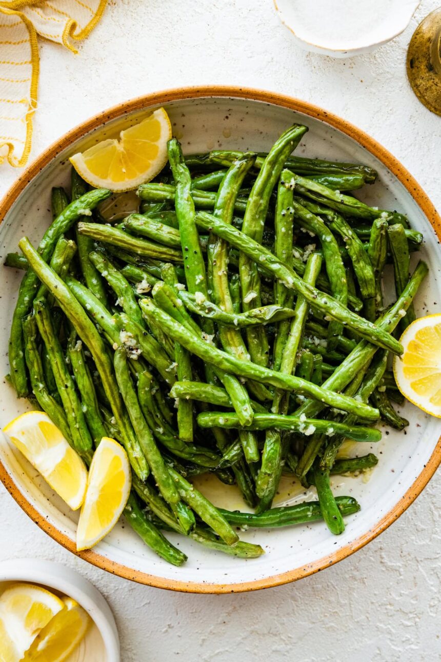 Roasted green beans in a large bowl with lemon wedges.