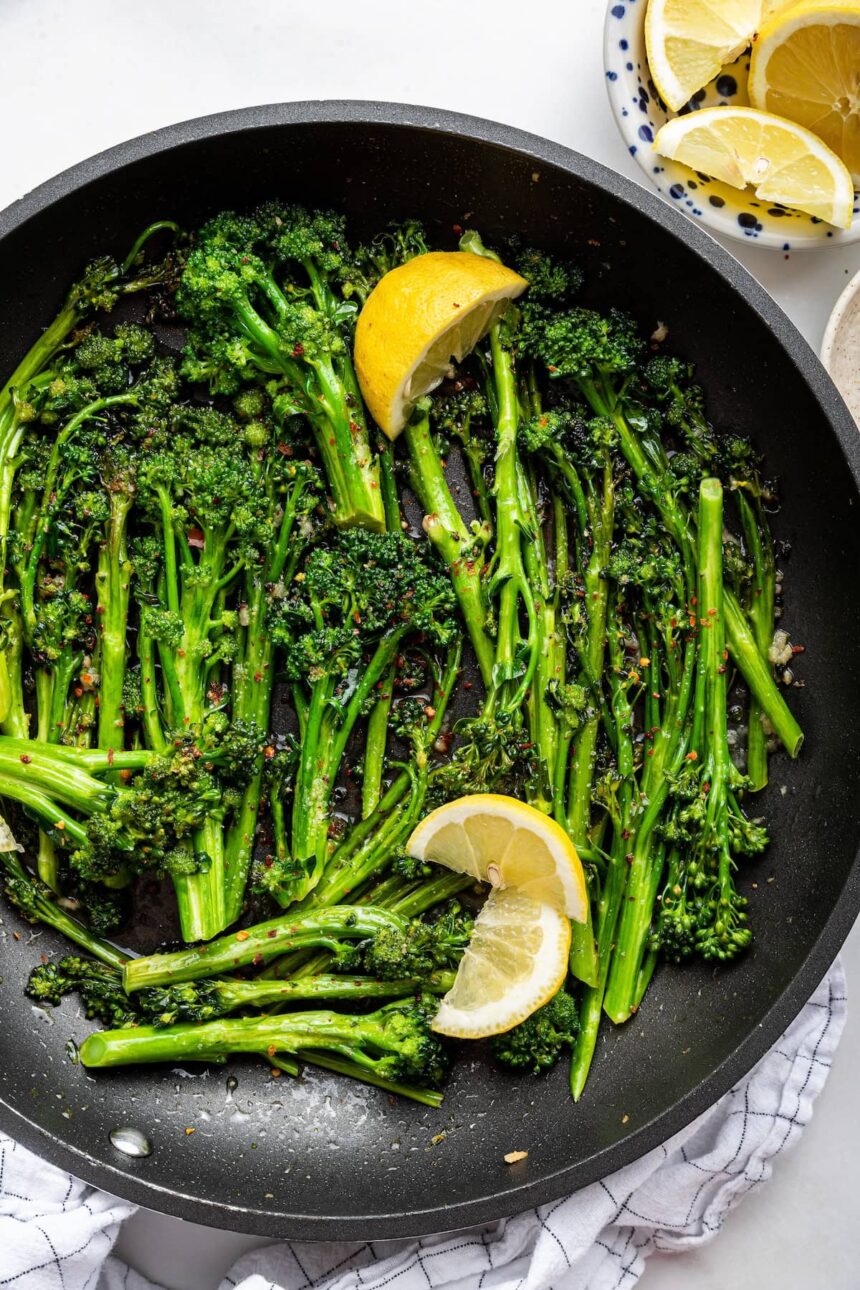 A pan of sautéed broccolini with lemon wedges and red pepper flakes.