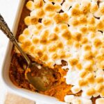 Sweet potato casserole in a square baking dish with a portion missing in the corner where a metal spoon is.