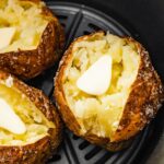 Three air fryer baked potatoes sliced open with butter in an air fryer.