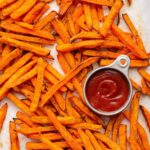 Sweet potato fries spread out near a small container of ketchup.