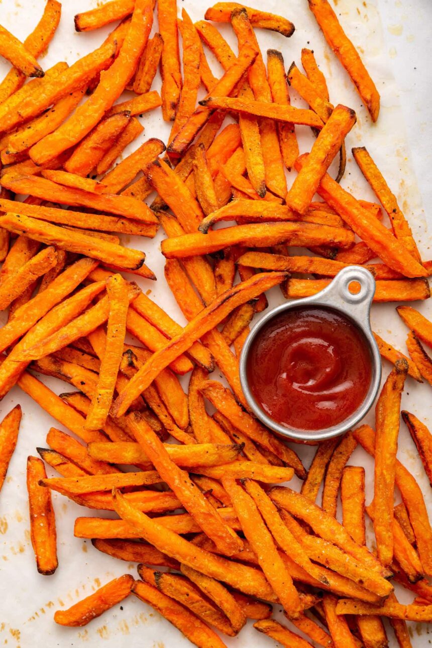 Sweet potato fries spread out near a small container of ketchup.