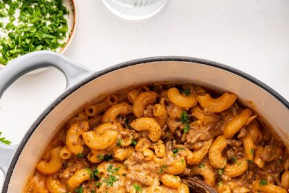 Healthy hamburger helper garnished with fresh herbs, in a large pot with a wooden serving spoon.