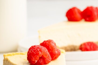 A slice of healthy cheesecake served on a white plate topped with fresh raspberries. A bite has been taken out of the slice.