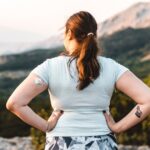 Woman wearing a CGM device near a ledge and looks out at the sunset.