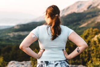 Woman wearing a CGM device near a ledge and looks out at the sunset.