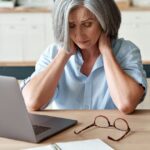 Woman in front of laptop holds her head in her hands.