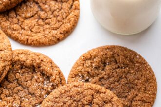 Multiple molasses cookies sprinkled with cane sugar with a glass of milk in the background.