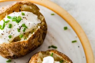 Three baked potatoes split open on a plate with sour cream, fresh chives, and seasoning.