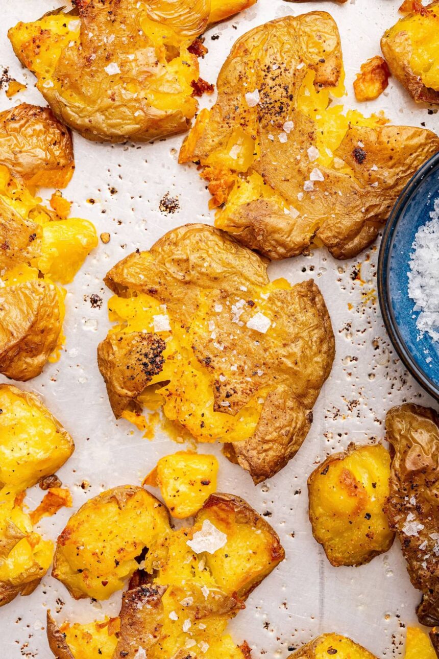 Seasoned and salted smashed potatoes on a baking tray.