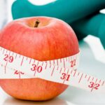 Measuring tape wrapped around a red apple with weights in the background