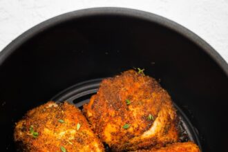 Four bone-in chicken thighs cooked in the basket of an air fryer topped with fresh parsley.