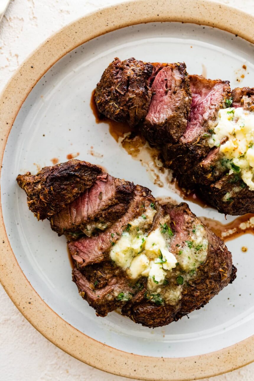 Two filet mignon pieces sliced on a white plate topped with garlic butter.