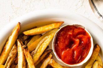 A plate of air fryer french fries with a small container of ketchup on the side.