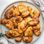 Baked boneless chicken thighs on a plate, garnished with fresh herbs.