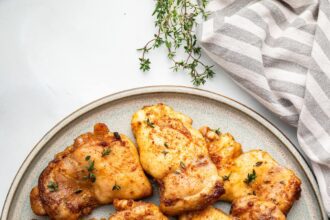 Baked boneless chicken thighs on a plate, garnished with fresh herbs.