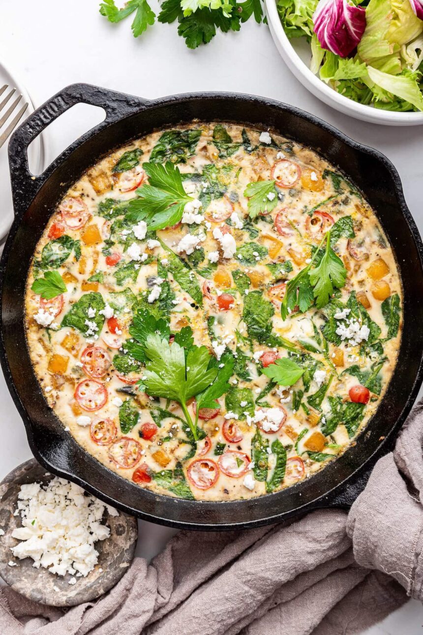 An egg white frittata in a cast iron skillet. The frittata is garnished with fresh herbs and feta cheese.