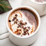 Two white mugs of hot chocolate topped with a little whip cream and chocolate shavings.