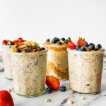 Four glass jars of overnight oats topped with fresh berries.