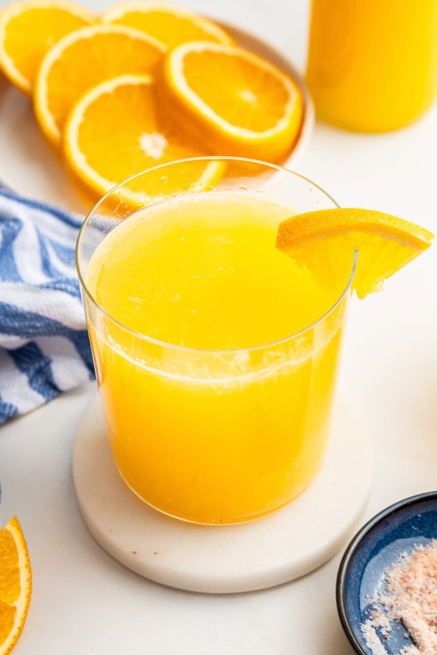 An adrenal cocktail in a glass with a clear straw in it. An orange slice is on the edge of the glass.