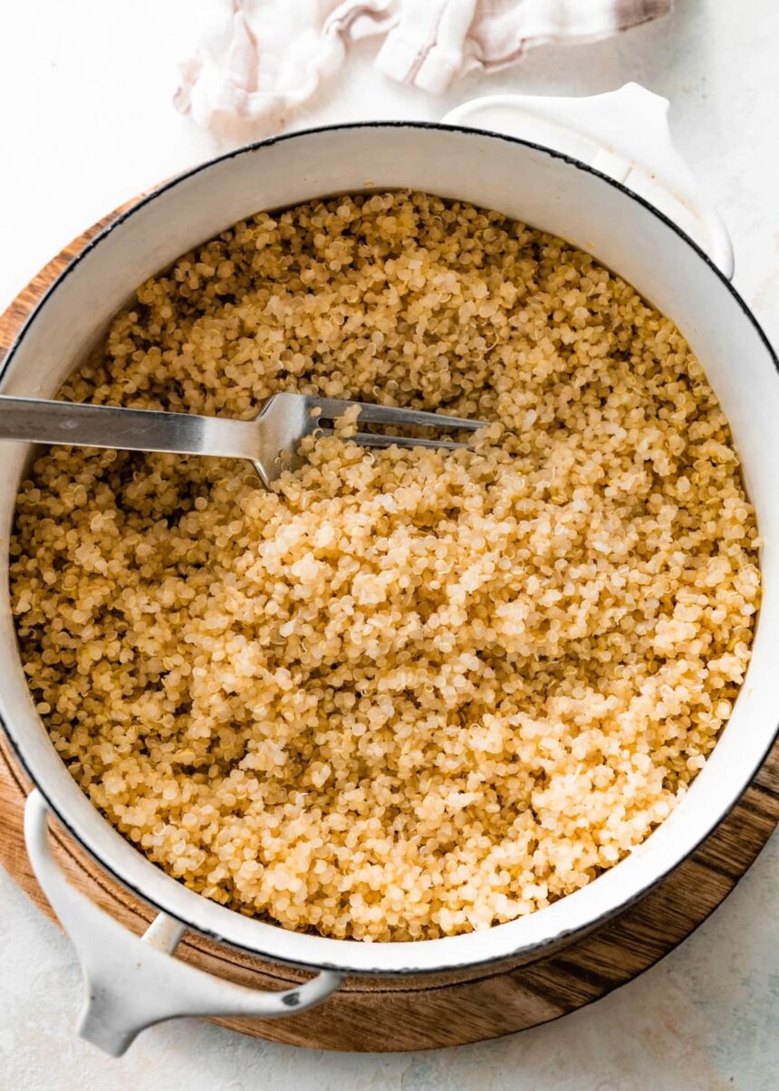 A large white pot filled with cooked quinoa. There is a silver fork in the quinoa.