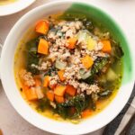 Sausage and kale soup served up in a green and white soup bowl.