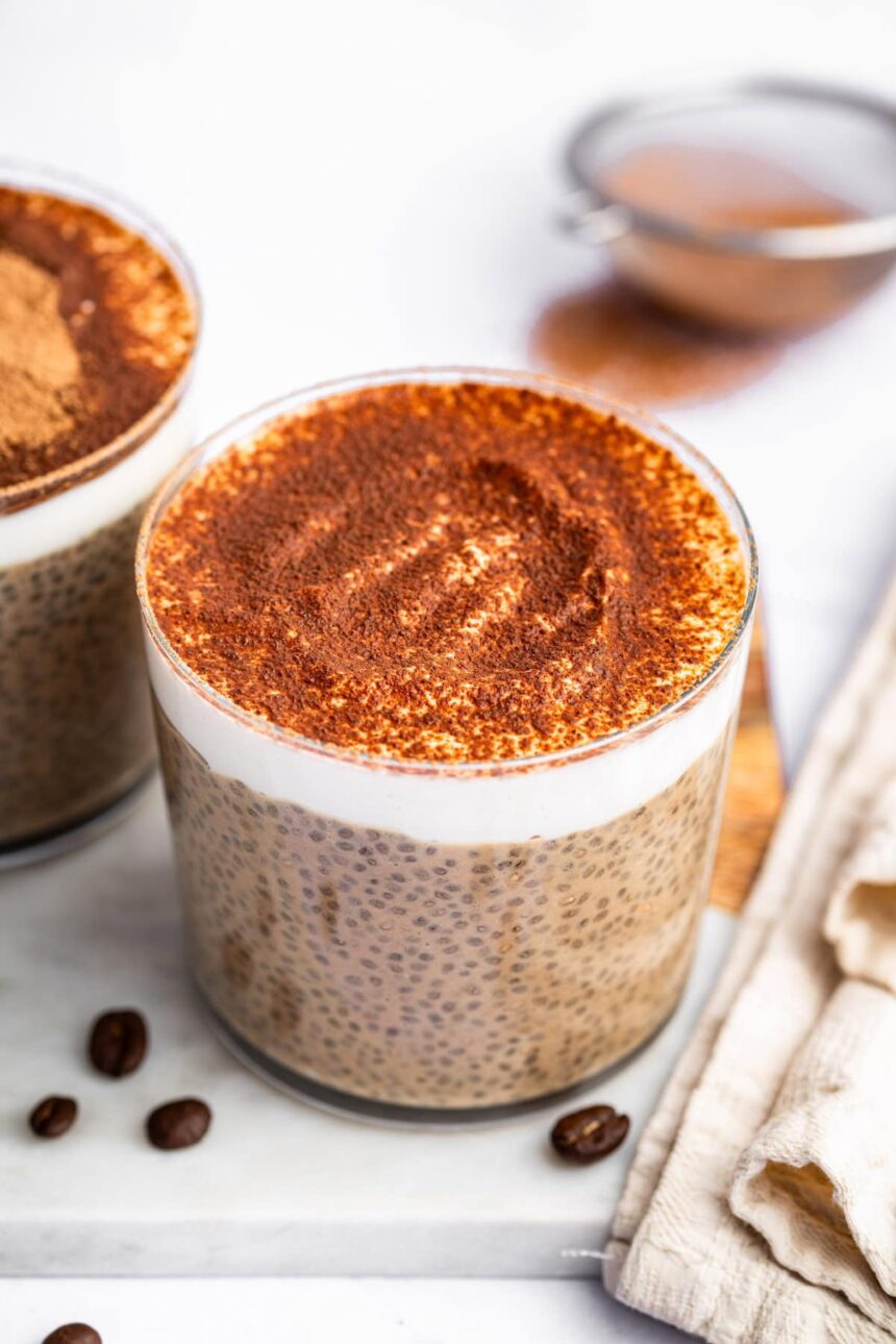 A glass cup of tiramisu chia pudding topped with cocoa powder.